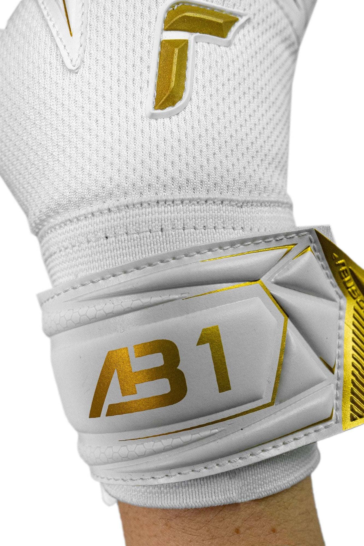Junior goalkeeper glove with a white textured knit backhand, gold logo and AB1 lettering, and a grey wraparound wrist strap.