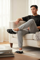 Man relaxing on couch wearing black and white hockey slippers with plush cushioning and non-slip sole